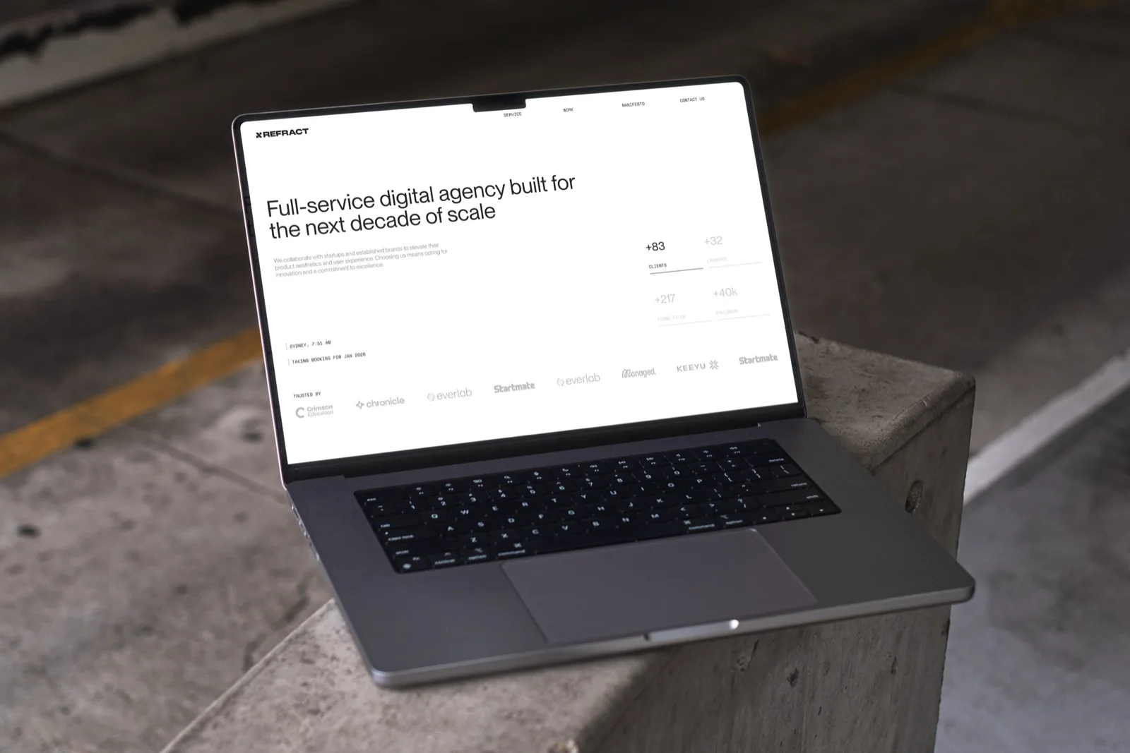 The same laptop showing the light-mode site: black type on white, the headline "Full-service digital agency built for the next decade of scale", with client logos along the foot.