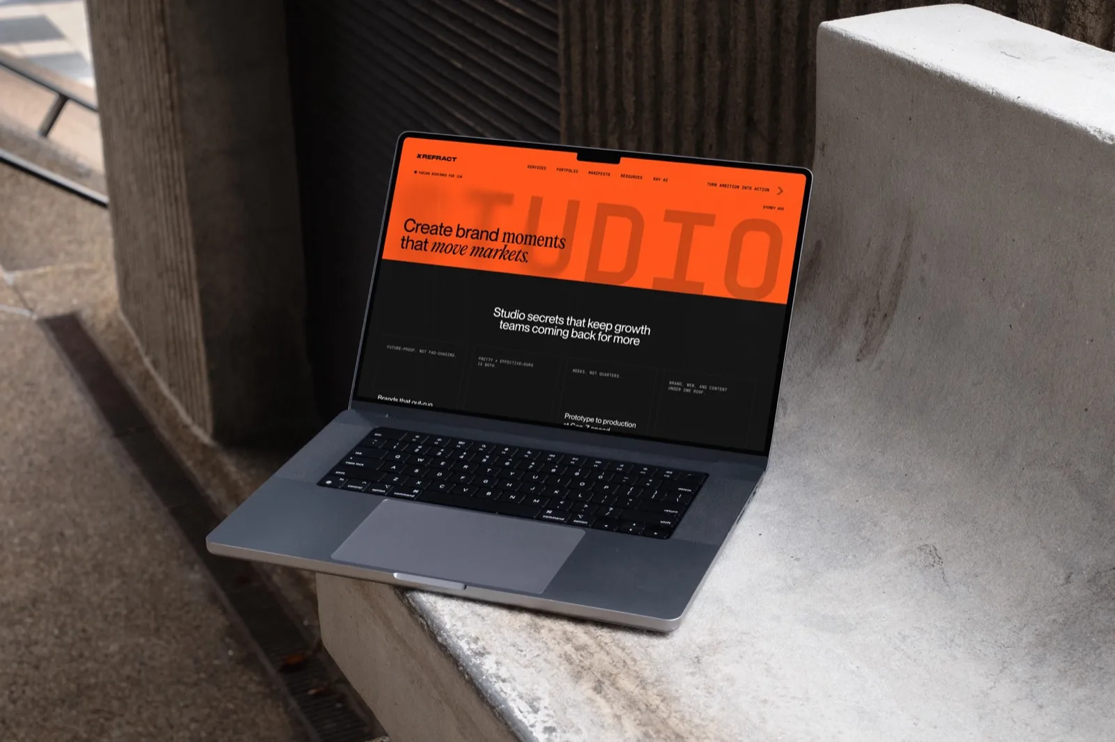 A laptop on a concrete ledge showing the orange Refract site, with a large STUDIO wordmark behind the headline "Create brand moments that move markets".