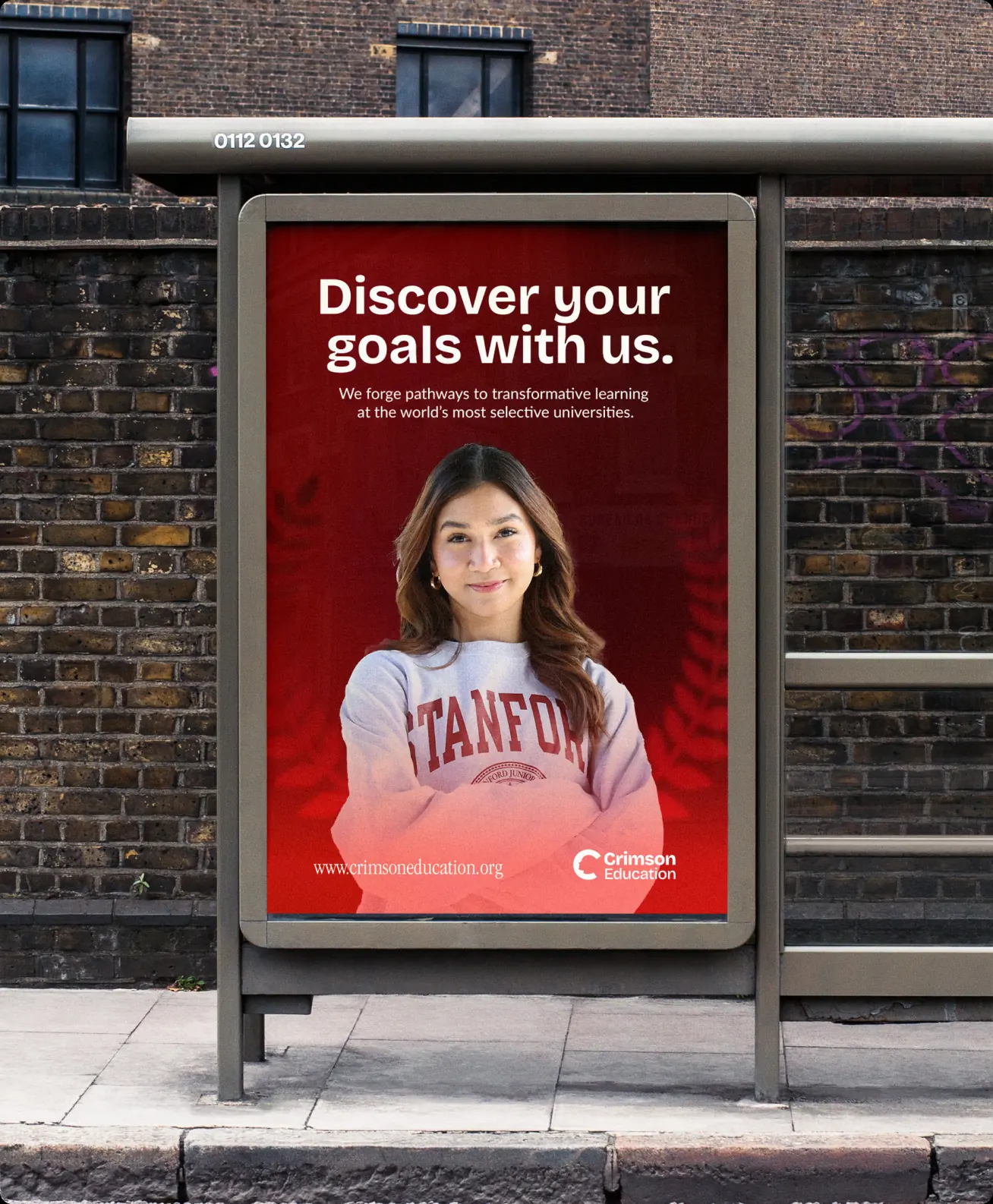 A bus-shelter poster on a brick street reading “Discover your goals with us. We forge pathways to transformative learning at the world’s most selective universities.”, over a student in a Stanford sweatshirt
