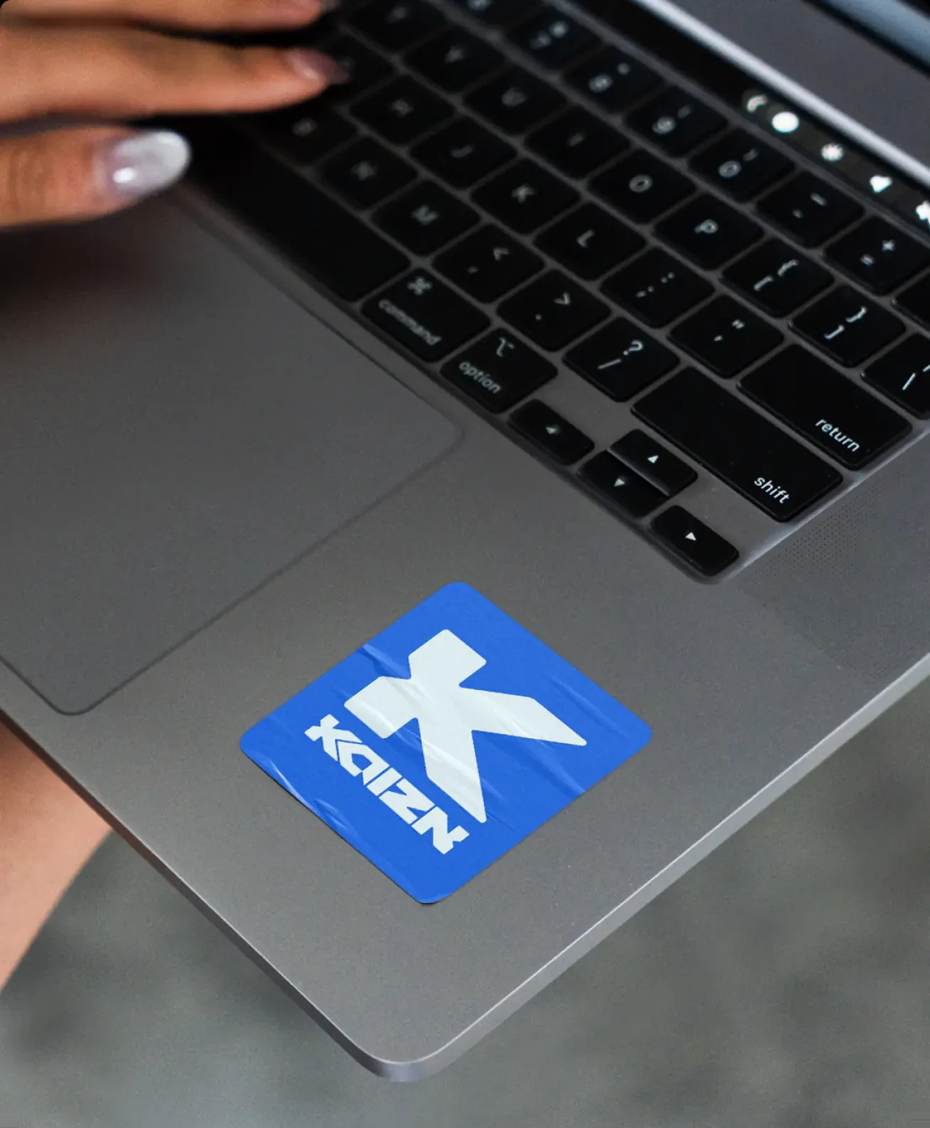 The K sticker on a laptop lid, under a hand at the keyboard