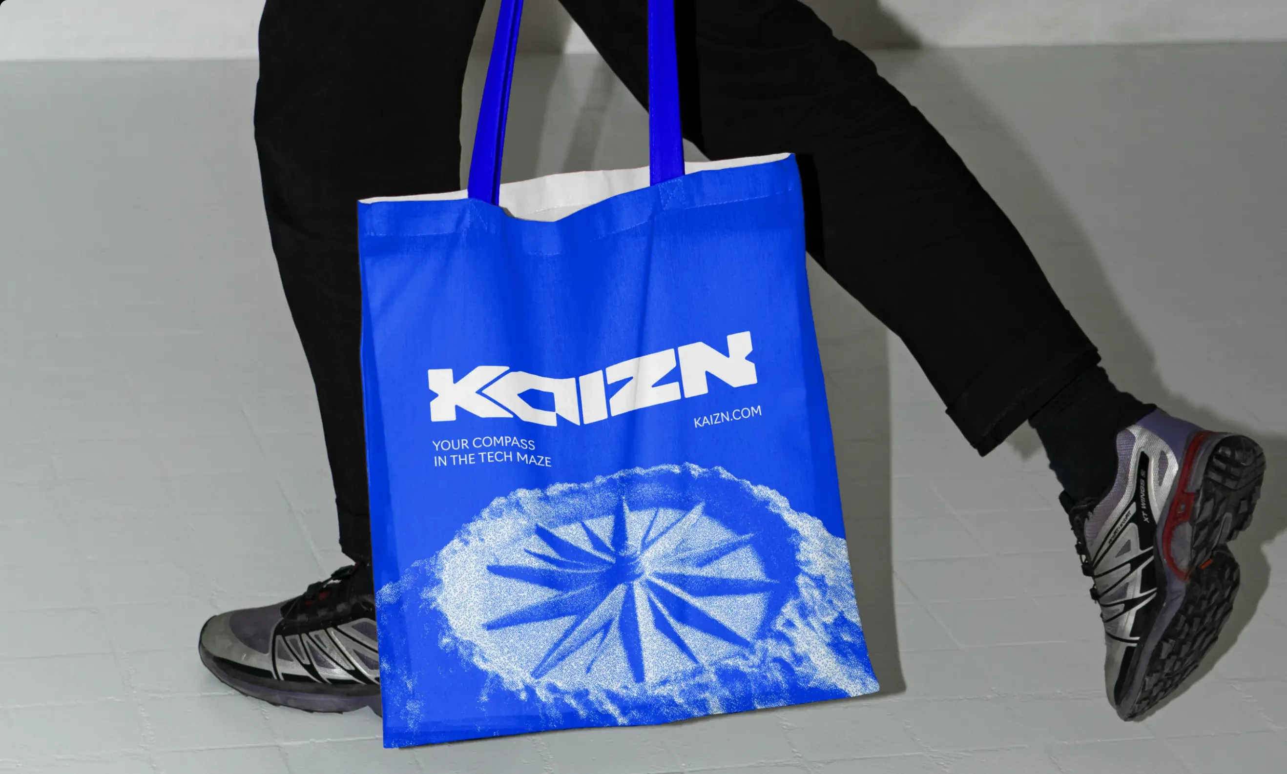 A blue Kaizn tote carried at the hip, shot against a pale wall