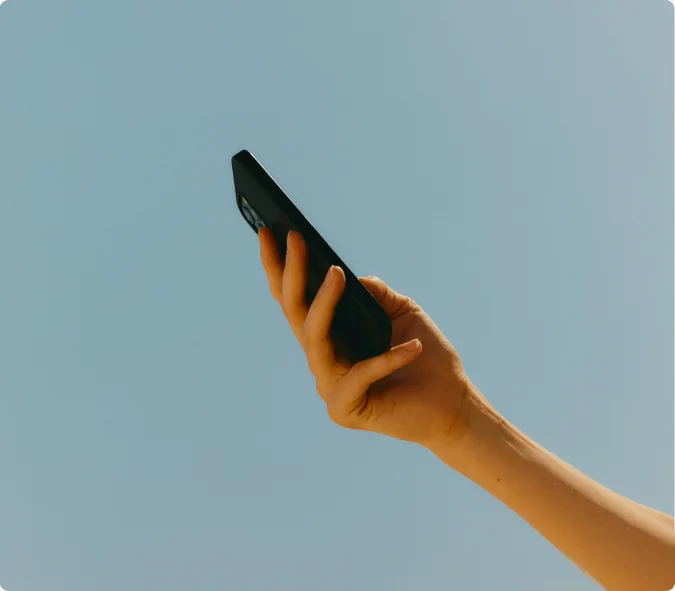 A hand holding a phone up against a clear sky