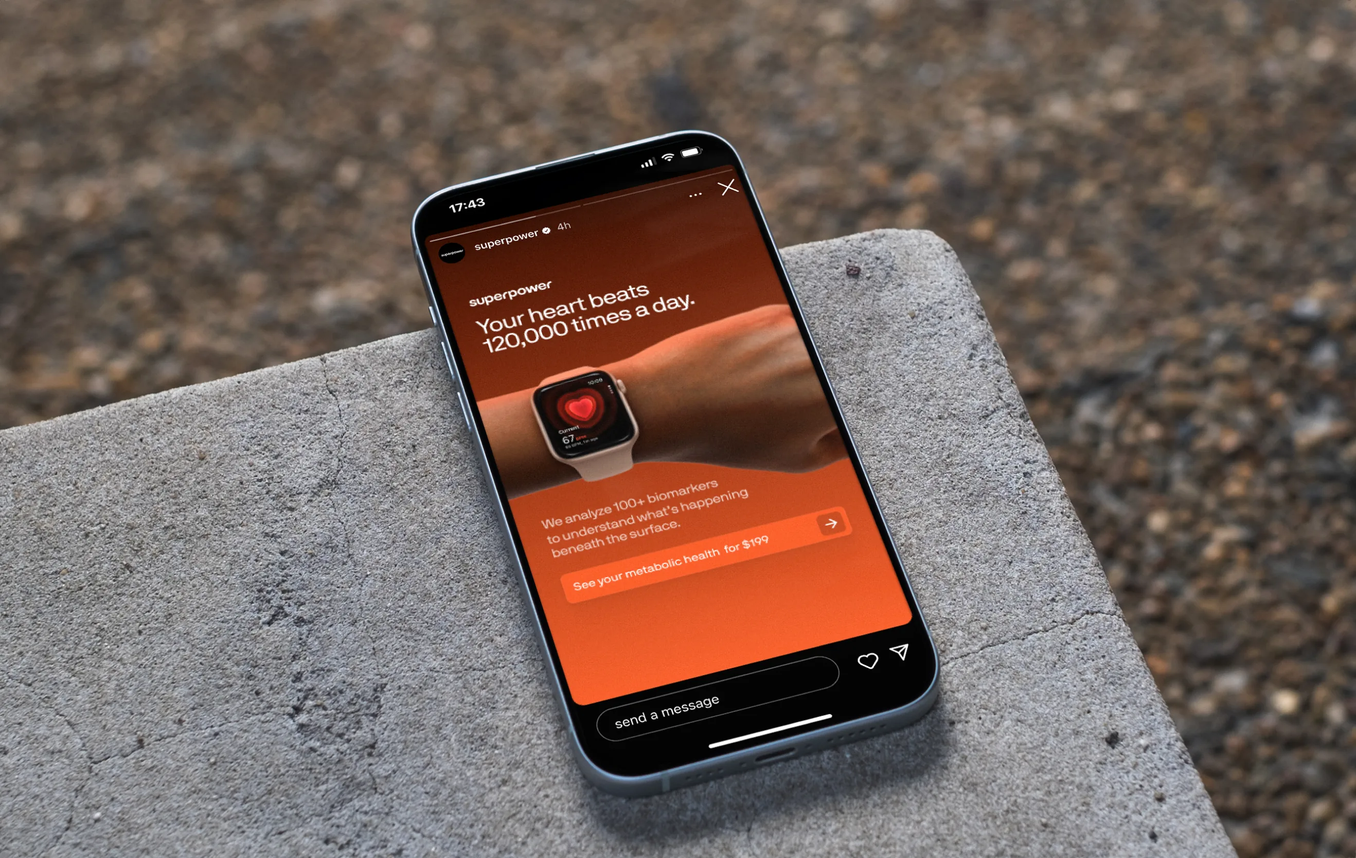 A phone lying on a concrete ledge over gravel, playing a Superpower Instagram story: “Your heart beats 120,000 times a day.” over a smartwatch showing a heart, with a “See your metabolic health for $199” button